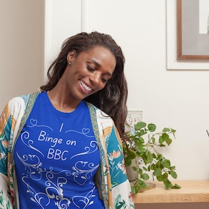 May include: A royal blue t-shirt with the text "I Binge on BBC" in white script and decorative flourishes. The shirt is part of a casual wear collection. The model is wearing a patterned kimono.