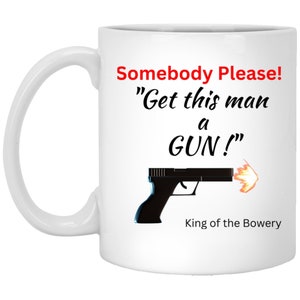 Puede incluir: Taza de cerámica blanca con un gráfico de pistola negra y el texto "Somebody Please! Get this man a GUN!" en negro y rojo. La frase "King of the Bowery" está impresa debajo del gráfico de la pistola.