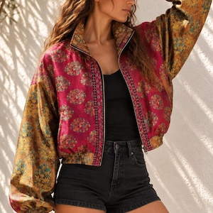 Può includere: Una giacca bomber con zip caratterizzata da un pannello centrale magenta vivace con un motivo floreale ripetuto, in contrasto con maniche color oro metallizzato con una stampa floreale abbinata. La giacca include un colletto alto, polsini a coste e una canotta nera.