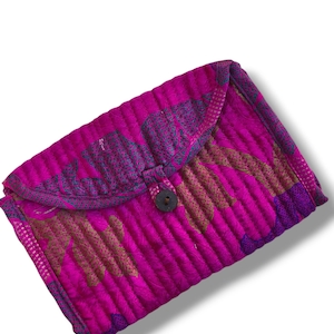 Op de afbeelding: Een rechthoekige gewatteerde clutch van fel magenta roze stof met een donkerpaars en goudkleurig bloemenpatroon. De tas heeft een overslagflap die wordt vastgezet met een enkele donkerbruine ronde knoop in het midden van de voorzijde.