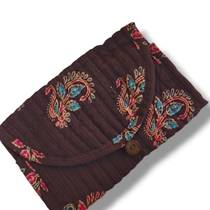 Op de afbeelding: Een donkerbruine gewatteerde portemonnee met een herhalend paisley-patroon in tinten blauwgroen, roze en oranje. De portemonnee heeft een afgeronde klepsluiting die wordt vastgezet met een kleine houten knoop en verticale stiksels.