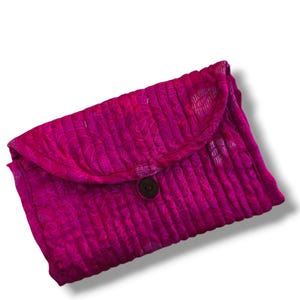 May include: A vibrant magenta clutch bag featuring a quilted texture with vertical stitching and a subtle paisley pattern. The rectangular accessory has a rounded flap closure secured by a single dark brown button centred on the front.