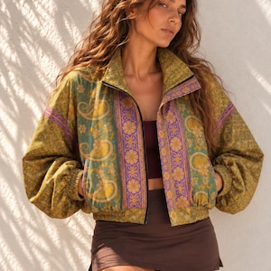 May include: A cropped zip-up jacket featuring a vibrant paisley and floral pattern in shades of olive green, mustard yellow, and purple. The jacket has a high collar, long sleeves with elastic cuffs, and a matching elastic waistband.