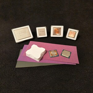 May include: A collection of computer processors in white plastic frames, including an AMD EPYC processor, an AMD Ryzen processor, and two Intel processors. The processors are on a purple and grey surface.