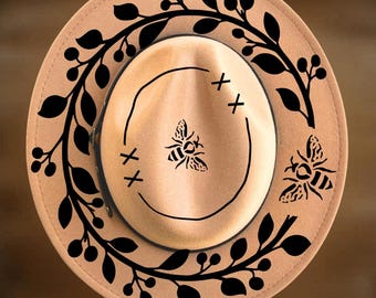 May include: A tan felt hat featuring black laser-cut designs of bees and leafy branches. The crown displays a central bee graphic with surrounding X marks. Text on the image reads For Hand Burning and CoolMoonDesigns.