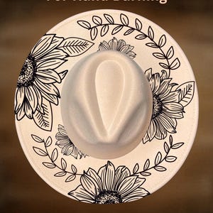 Puede incluir: Sombrero fedora color crema con ala ancha, con un diseño floral negro de girasoles y hojas. El texto "For Hand Burning" y "CoolMoonDesigns" está impreso en el sombrero.