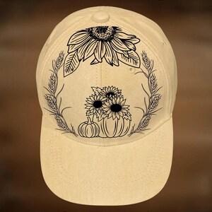 May include: A beige baseball cap with a black floral and pumpkin design. The cap features the text "For Hand Burning" and "CoolMoonDesigns". The design includes a sunflower, wheat stalks, and pumpkins.