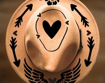 May include: A tan fedora hat featuring black graphic designs including a central heart, surrounding arrows, a flower at the top, and wings at the bottom. The text "For Hand Burning" appears at the top and "CoolMoonDesigns" at the bottom.