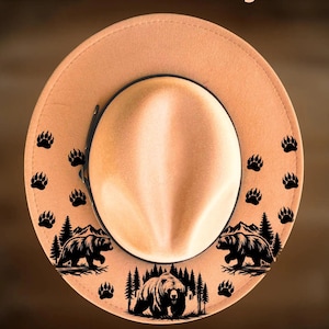 Può includere: Cappello fedora color beige con fascia nera. Il cappello presenta disegni neri di orsi e impronte di zampe sul bordo. Il testo "For Hand Burning" e "CoolMoonDesigns" è stampato sull'immagine.