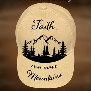 Può includere: Cappellino da baseball beige con le parole "Faith" e "can move Mountains" in corsivo nero. Una silhouette nera di montagne e alberi è sotto la parola "Faith". Il testo "For Hand Burning" e "CoolMoonDesigns" è anche sul cappellino.