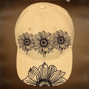 May include: Tan baseball cap with a black sunflower design. The cap features three sunflowers across the front and one on the brim. Text on the cap reads "For Hand Burning" and "CoolMoonDesigns".