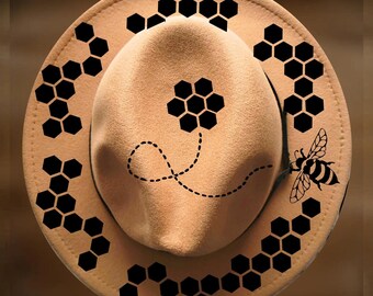May include: A tan felt hat featuring black honeycomb patterns, a bee illustration, and a dotted flight path. The text "For Hand Burning" appears at the top, and "CoolMoonDesigns" is printed at the bottom of the image.