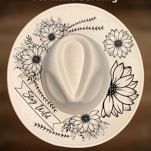 May include: A cream-coloured fedora hat featuring black line art of sunflowers and foliage. A banner on the left side contains the text "Stay Wild". The text "For Hand Burning" appears at the top and "CoolMoonDesigns" at the bottom.