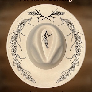 Può includere: Un cappello a tesa larga color crema con disegni a linee nere di spighe di grano disposte in un motivo circolare sulla tesa e una singola spiga sulla calotta. Il testo "For Hand Burning" e "CoolMoonDesigns" è visibile nell'immagine.
