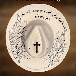 May include: A cream-colored fedora hat with a black cross and feather design. The hat features the text "He will cover you with His feathers Psalm 91:4" and "For Hand Burning" and the brand name "CoolMoonDesigns".