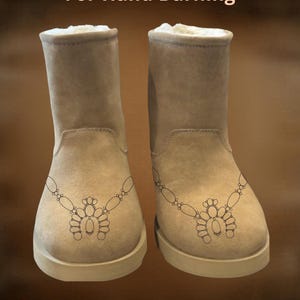 Könnte beinhalten: Ein Paar beige Wildlederstiefel mit einem dekorativen Design auf der Vorderseite. Die Stiefel haben ein cremefarbenes Futter und eine dicke Sohle. Der Text "For Hand Burning" und "CoolMoonDesigns" sind sichtbar.