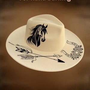 May include: Cream-colored cowboy hat with a black horse head design, arrows, and horseshoe accents. The hat features the text "For Hand Burning" and "CoolMoonDesigns".