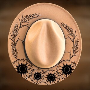 Könnte beinhalten: Ein beigefarbener Fedora-Hut mit schwarzen Linienzeichnungen von Sonnenblumen und Weizenähren auf der Krempe. Der Text For Hand Burning steht oben, CoolMoonDesigns unten. Der Hut hat eine mittige Vertiefung in der Hutkrone.