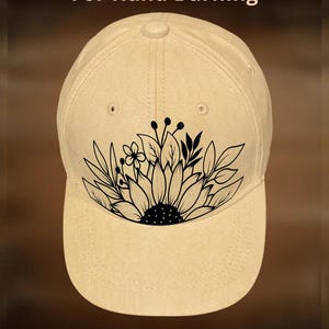 May include: A beige baseball cap featuring a black sunflower design. The text "For Hand Burning" is above the cap, and "CoolMoonDesigns" is below. The cap has a curved peak and a button on top.