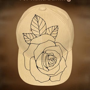 May include: Cream-colored baseball cap featuring a black outline of a rose and leaves. The text "For Hand Burning" and "CoolMoonDesigns" are displayed on the cap. This cap is a unique accessory for those interested in hand-burning art.