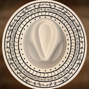 May include: A cream-colored fedora hat with a decorative black border. The border features a repeating pattern of geometric shapes and leaf designs. The hat has a classic teardrop crown and a wide brim, perfect for sun protection.