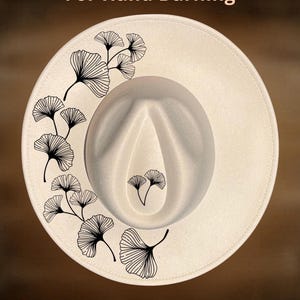 May include: Cream-colored fedora hat with black ginkgo leaf design. The hat features the text "For Hand Burning" and "CoolMoonDesigns". The hat is a stylish accessory.