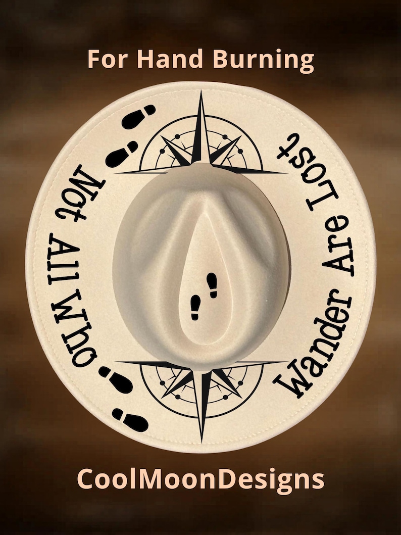 May include: A cream-colored fedora hat with a wide brim. The hat features black text and graphics, including a compass rose, footprints, and the phrases "Not All Who Wander Are Lost" and "For Hand Burning". The brand name "CoolMoonDesigns" is also visible.