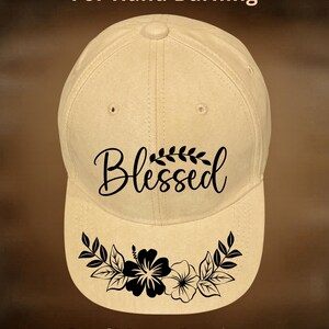 May include: A beige baseball cap featuring the text "For Hand Burning" at the top, the word "Blessed" in black script with a leaf accent in the center, a black floral graphic on the brim, and the text "CoolMoonDesigns" at the bottom.
