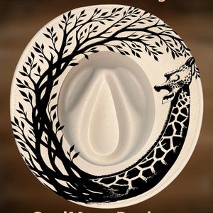Può includere: Cappello fedora color crema con un design di giraffa nera e un bordo di rami di albero. Il cappello presenta il testo "For Hand Burning" e "CoolMoonDesigns".