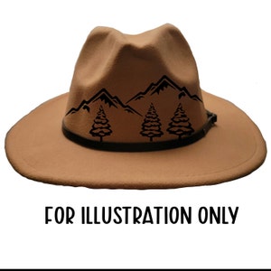 May include: A tan fedora-style hat with a black mountain and tree design. The hat has a black leather band and a wide brim. The text "FOR ILLUSTRATION ONLY" is printed in black at the bottom of the image.