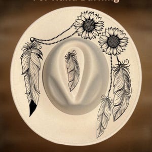 May include: Cream-coloured fedora hat with black sunflower and feather designs. The hat features the text "For Hand Burning" and "CoolMoonDesigns". The hat has a wide brim and a centre crease.