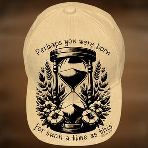 May include: A beige baseball cap featuring a black hourglass design with floral accents and the text "Perhaps you were born for such a time as this" from Esther 4:14. The cap has a curved brim and a classic six-panel design.