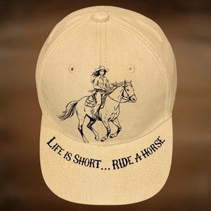 May include: A beige baseball cap with a black graphic of a person riding a horse. The text "LIFE IS SHORT... RIDE A HORSE" is arched across the front. The words "For Hand Burning" and "CoolMoonDesigns" are also visible.