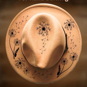 Puede incluir: Sombrero fedora color beige con un diseño de diente de león negro. El sombrero tiene un ala ancha y una corona redondeada. El texto "For Hand Burning" y "CoolMoonDesigns" están impresos en la imagen.