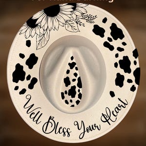 Peut inclure: Chapeau fedora crème avec des taches de vache noires et un motif de tournesol. Le chapeau porte l'inscription "Well Bless Your Heart" et "CoolMoonDesigns". Le chapeau est conçu pour le hand burning.