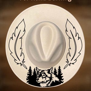 May include: Cream-colored fedora hat with a wolf and feather design. The hat features a black wolf illustration with pine trees and two black feather designs. The text "For Hand Burning" and "CoolMoonDesigns" are also visible.