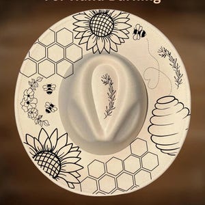 May include: A cream-coloured fedora hat featuring black line art illustrations of sunflowers, honeycombs, bees, a beehive, and floral sprigs. The text "For Hand Burning" appears at the top and "CoolMoonDesigns" is printed at the bottom.