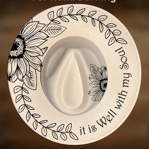 May include: A cream-coloured fedora hat featuring black line art of sunflowers and leafy vines. The text "it is Well with my Soul" is printed in black script. The words "For Hand Burning" and "CoolMoonDesigns" appear above and below the hat.
