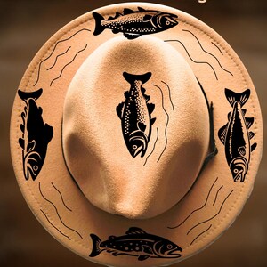 May include: Tan fedora hat with black fish designs and the text "For Hand Burning" and "CoolMoonDesigns". The hat features five fish illustrations and wavy lines, suitable for hand burning.