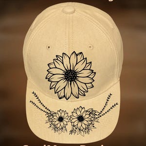 May include: A tan baseball cap with a black sunflower design on the front. The brim features two smaller sunflower designs with leaf accents. The text "For Hand Burning" and "CoolMoonDesigns" are also visible.