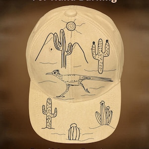 Può includere: Cappellino da baseball beige con un design a tema deserto. Il cappellino presenta un disegno a tratto nero di un roadrunner, cactus, montagne e un sole. Il testo "For Hand Burning" e "CoolMoonDesigns" è stampato.