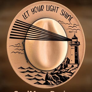 May include: Tan fedora hat with a lighthouse design. The hat features the text "Let Your Light Shine" and "Matt 5:16". The design includes a lighthouse, waves, and the words "For Hand Burning" and "CoolMoonDesigns".