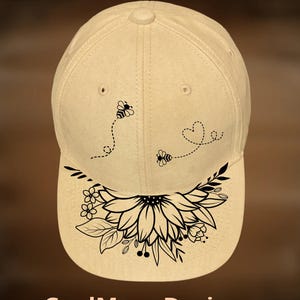 May include: A beige baseball cap featuring the text For Hand Burning at the top and CoolMoonDesigns at the bottom. The cap displays a black line art graphic of two bees with dotted flight paths and a large sunflower with leaves and small flowers.