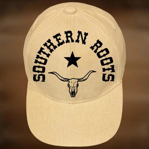 May include: A beige baseball cap with the words "SOUTHERN ROOTS" in a curved black font, a black star, and a bull skull graphic. The text "For Hand Burning" and "CoolMoonDesigns" are also visible.