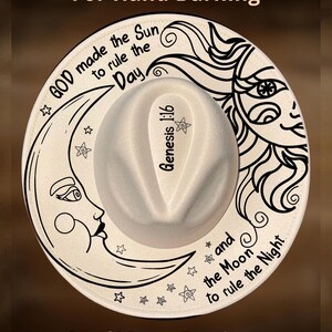 May include: White fedora hat with a black and white celestial design. The brim features a crescent moon, stars, and the text "GOD made the Sun to rule the Day." The crown has the text "Genesis 1:16". The hat also has a sun design and the text "and the Moon to rule the Night."