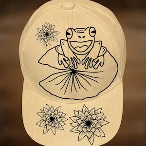 May include: Tan baseball cap with a black frog design on the front, along with two floral designs and the text "CoolMoonDesigns". The text "For Hand Burning" is above the frog design.