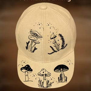 May include: A beige baseball cap with black mushroom illustrations and the text "For Hand Burning" and "CoolMoonDesigns". The cap features a curved brim and a button on top, with various mushroom designs.