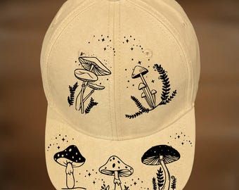 Puede incluir: Gorra de béisbol beige con ilustraciones de hongos negros y el texto "For Hand Burning" y "CoolMoonDesigns". La gorra presenta una visera curva y un botón en la parte superior, con varios diseños de hongos.