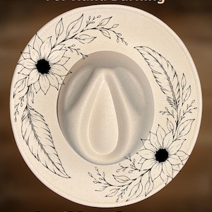 May include: A cream-colored fedora hat featuring black line art illustrations of sunflowers, leaves, and feathers. The text "For Hand Burning" appears at the top, and "CoolMoonDesigns" is printed at the bottom of the image.
