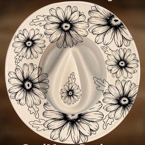 May include: A cream-colored fedora hat featuring black line art illustrations of daisies around the crown and brim. The text "For Hand Burning" appears at the top and "CoolMoonDesigns" at the bottom in a light peach font color.